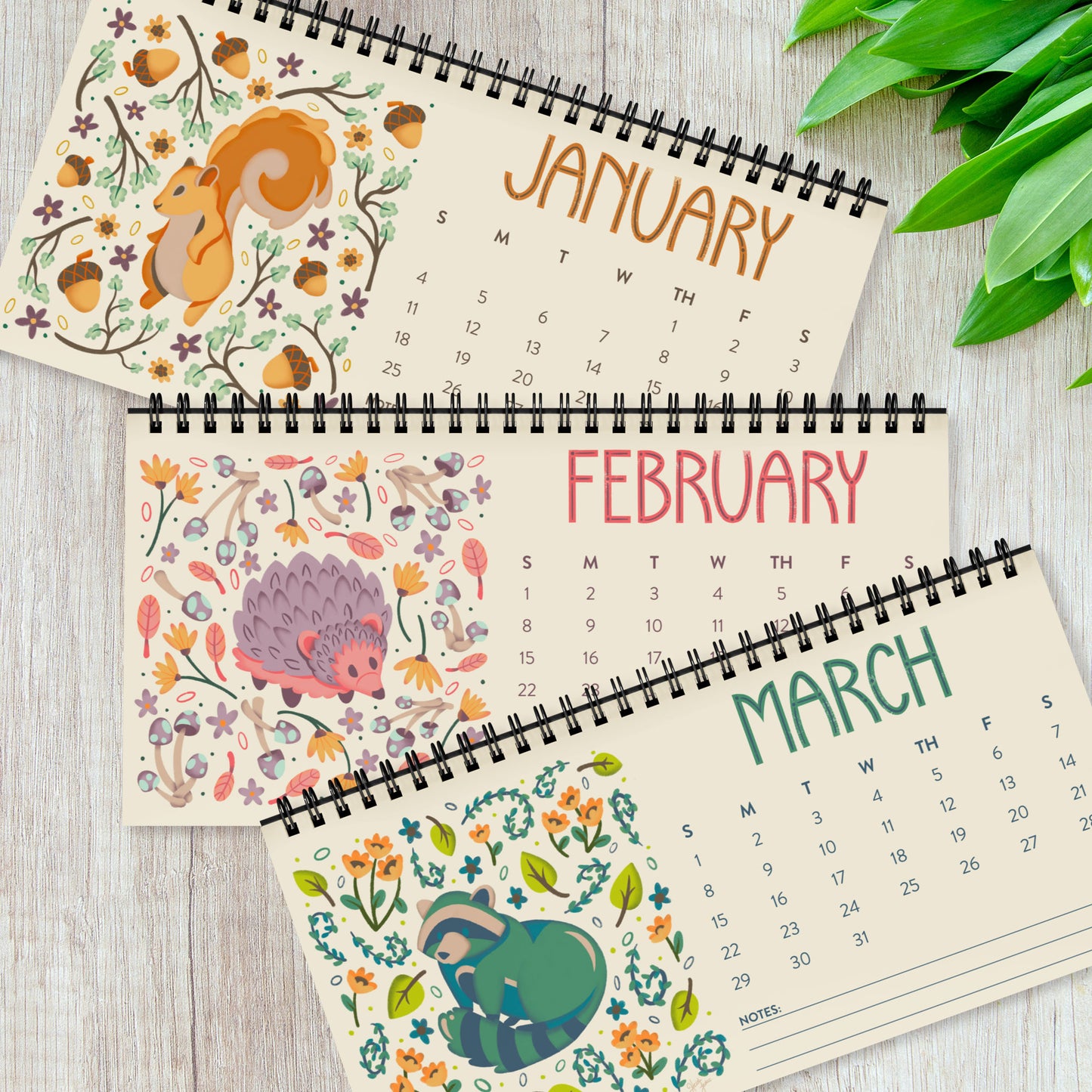 Three months from the 2026 desk calendar displayed together, each featuring a unique folk-art animal illustration printed on smooth satin paper. The monthly pages show vibrant artwork, clear date grids, and black spiral binding at the top. This set of quarterly pages highlights the high-quality printing and cohesive visual style of the calendar, ideal for buyers looking for a colourful, small standing desk calendar with illustrated animal art for 2026.