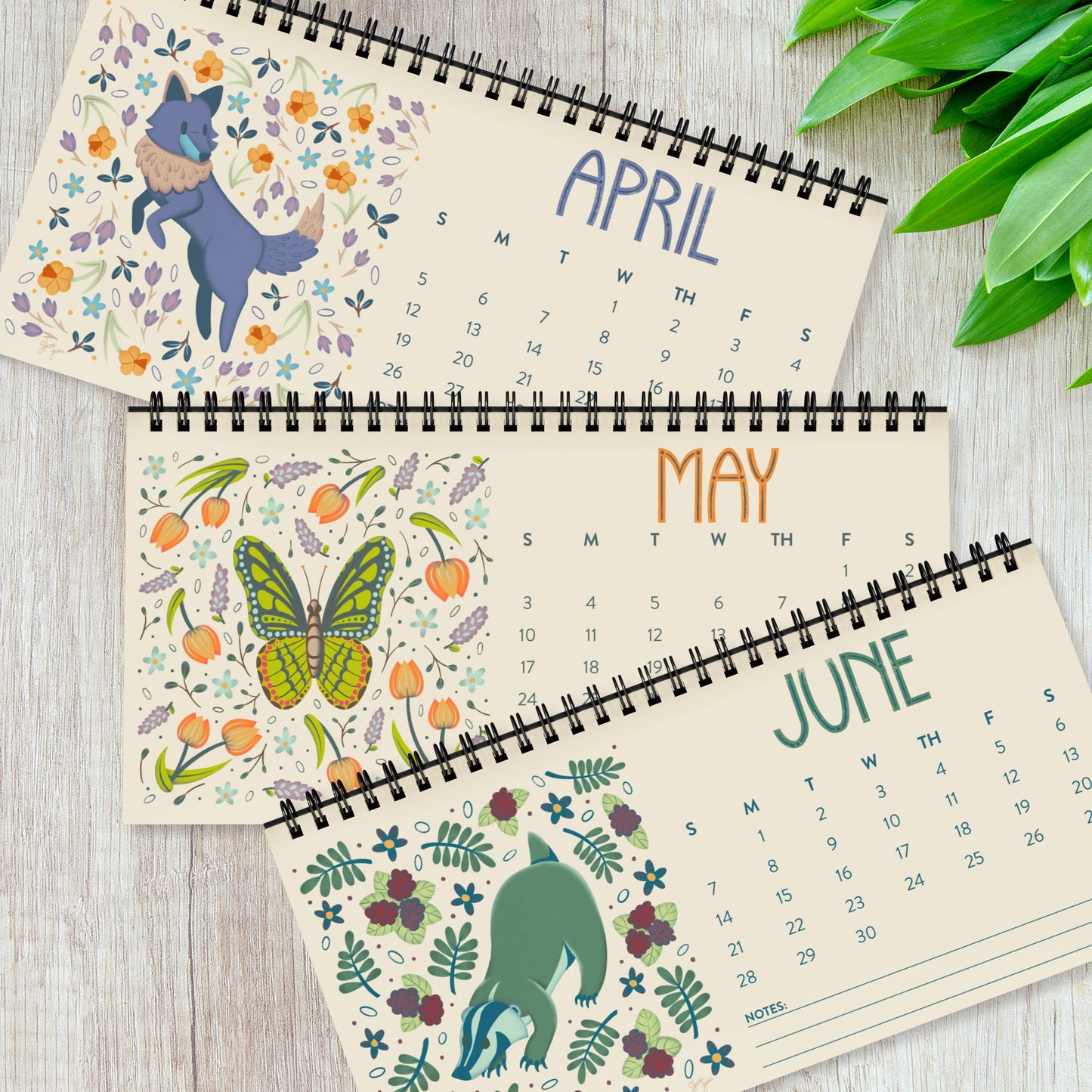 Three months from the 2026 desk calendar displayed together, each featuring a unique folk-art animal illustration printed on smooth satin paper. The monthly pages show vibrant artwork, clear date grids, and black spiral binding at the top. This set of quarterly pages highlights the high-quality printing and cohesive visual style of the calendar, ideal for buyers looking for a colourful, small standing desk calendar with illustrated animal art for 2026.