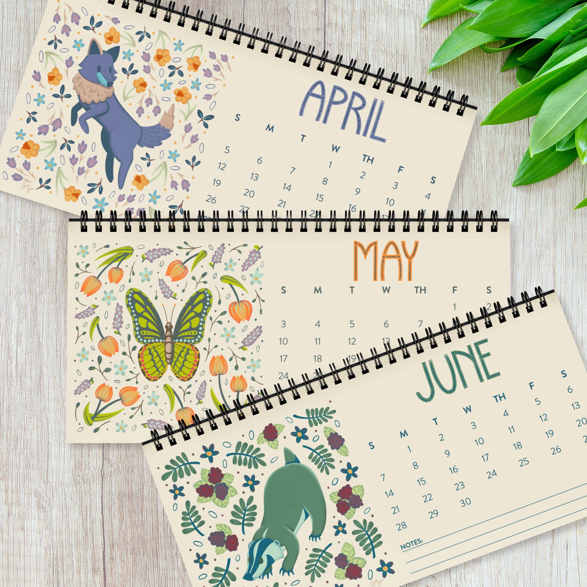 Three months from the 2026 desk calendar displayed together, each featuring a unique folk-art animal illustration printed on smooth satin paper. The monthly pages show vibrant artwork, clear date grids, and black spiral binding at the top. This set of quarterly pages highlights the high-quality printing and cohesive visual style of the calendar, ideal for buyers looking for a colourful, small standing desk calendar with illustrated animal art for 2026.