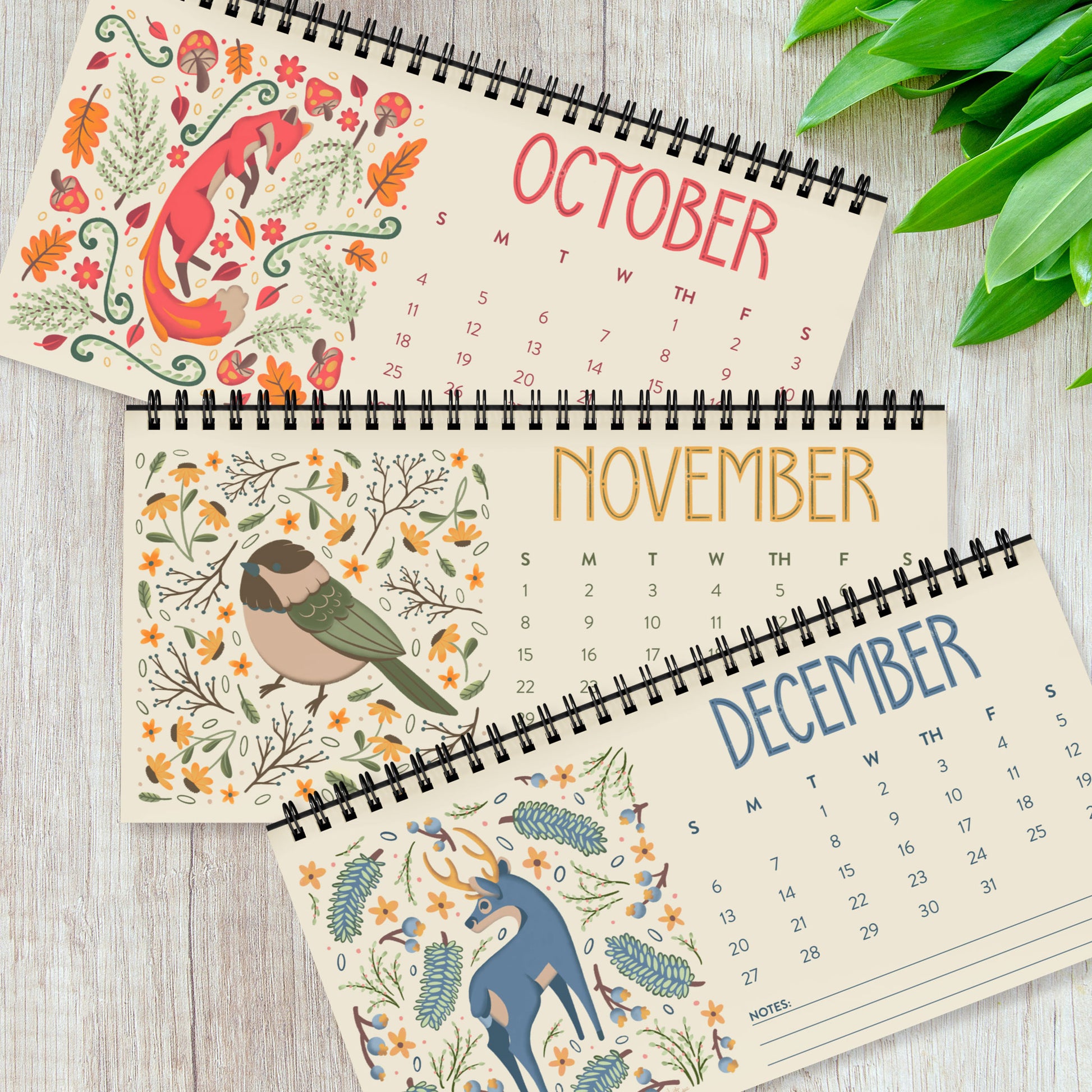 Three months from the 2026 desk calendar displayed together, each featuring a unique folk-art animal illustration printed on smooth satin paper. The monthly pages show vibrant artwork, clear date grids, and black spiral binding at the top. This set of quarterly pages highlights the high-quality printing and cohesive visual style of the calendar, ideal for buyers looking for a colourful, small standing desk calendar with illustrated animal art for 2026.