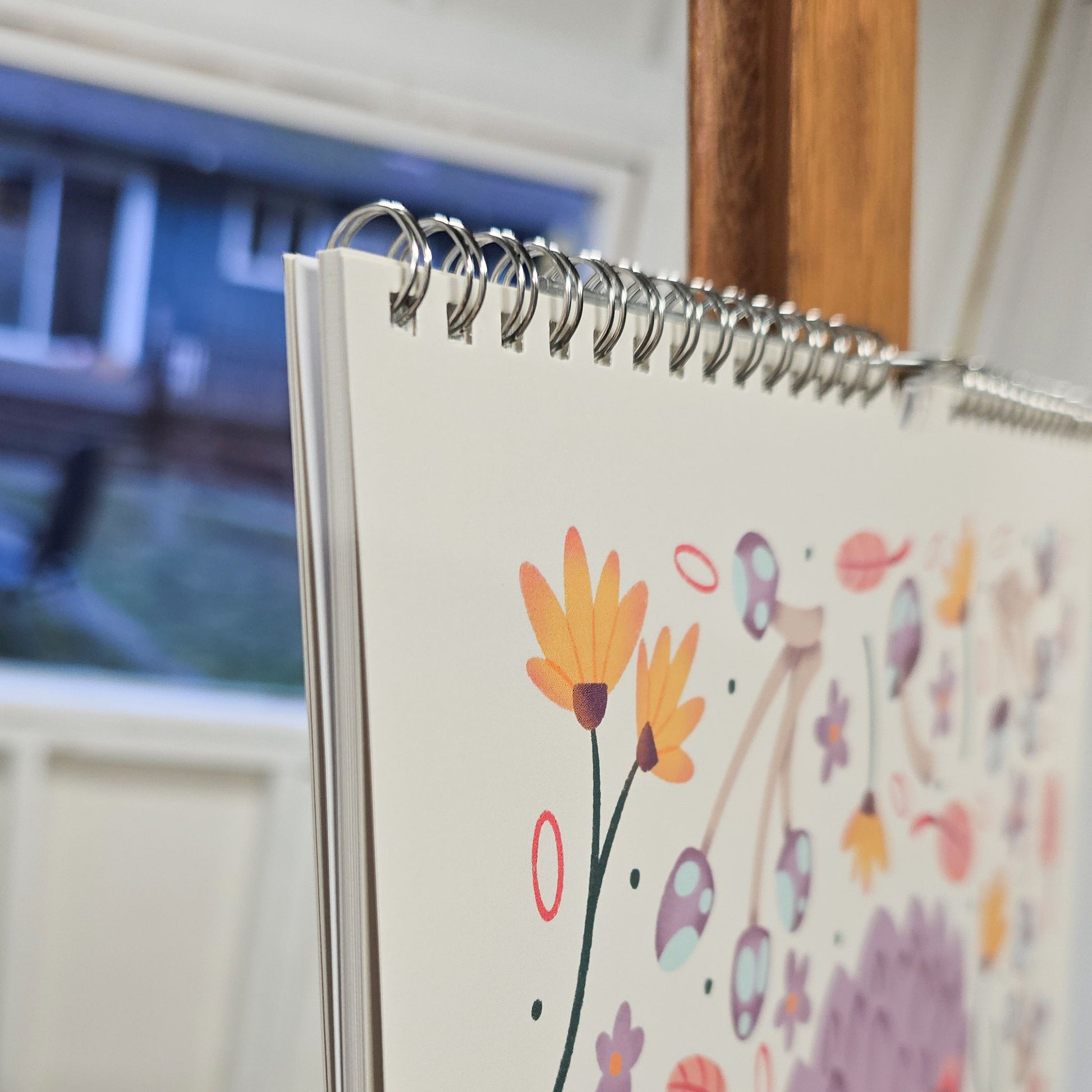 Close up of a spiral bound 2026 wall calendar featuring colourful folk-art animal illustrations. Wire-bound with premium thick paper, this illustrated monthly calendar showcases vibrant artwork for each month. Ideal for shoppers looking for a 2026 calendar, animal art calendar, home décor calendar, or unique artist-designed wall calendar.