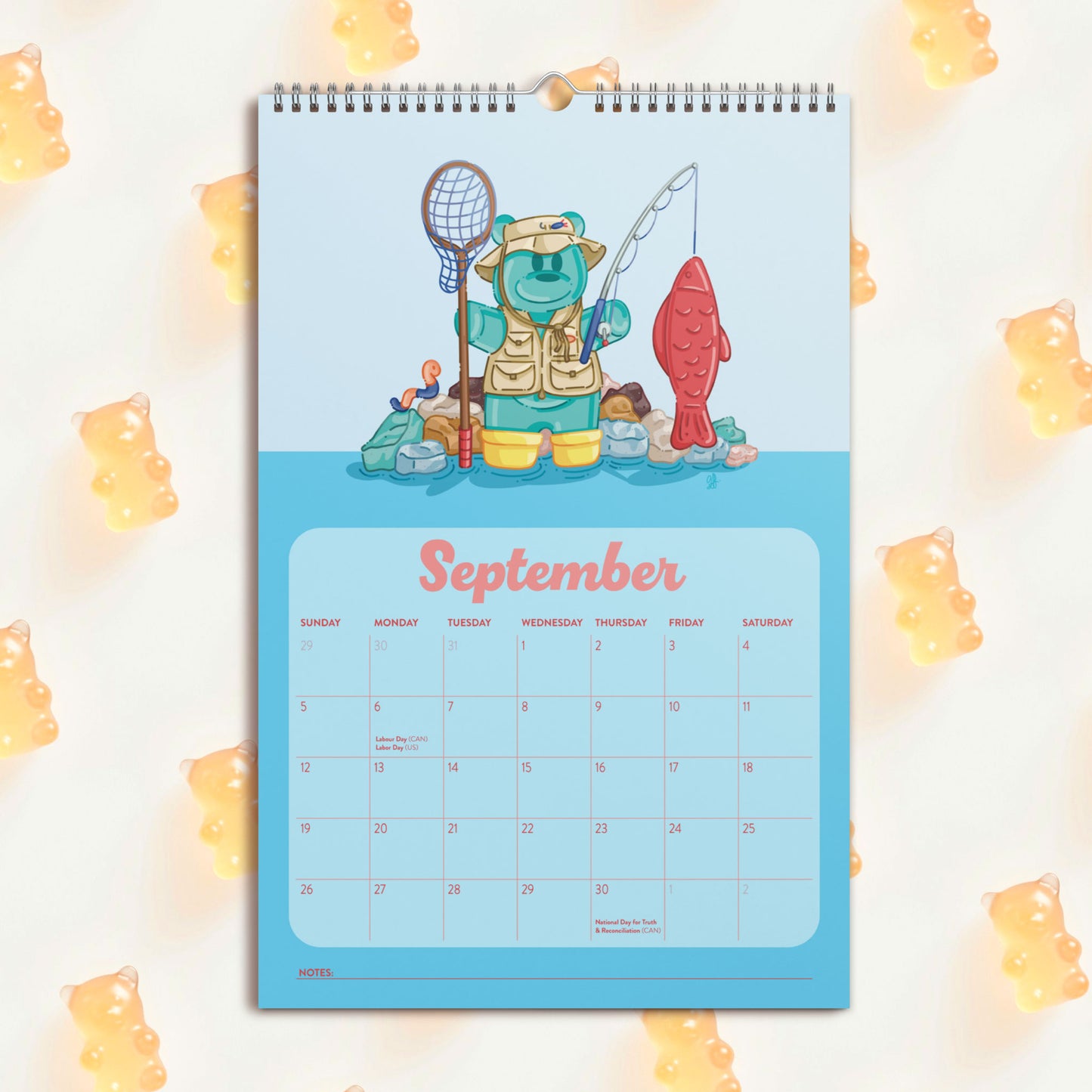 A spiral-bound September desk calendar featuring a teal gummy bear fishing with a swedish fish , set against a light background with scattered yellow gummy bear decorations.