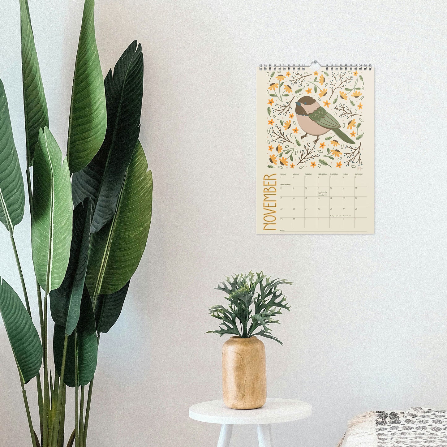 2026 wire-bound wall calendar hanging on a neutral wall, displaying colourful folk-art animal artwork and a clear monthly layout. Ideal for home offices, kitchens, studios, classrooms, or anyone looking for a decorative illustrated 2026 wall calendar with unique art.