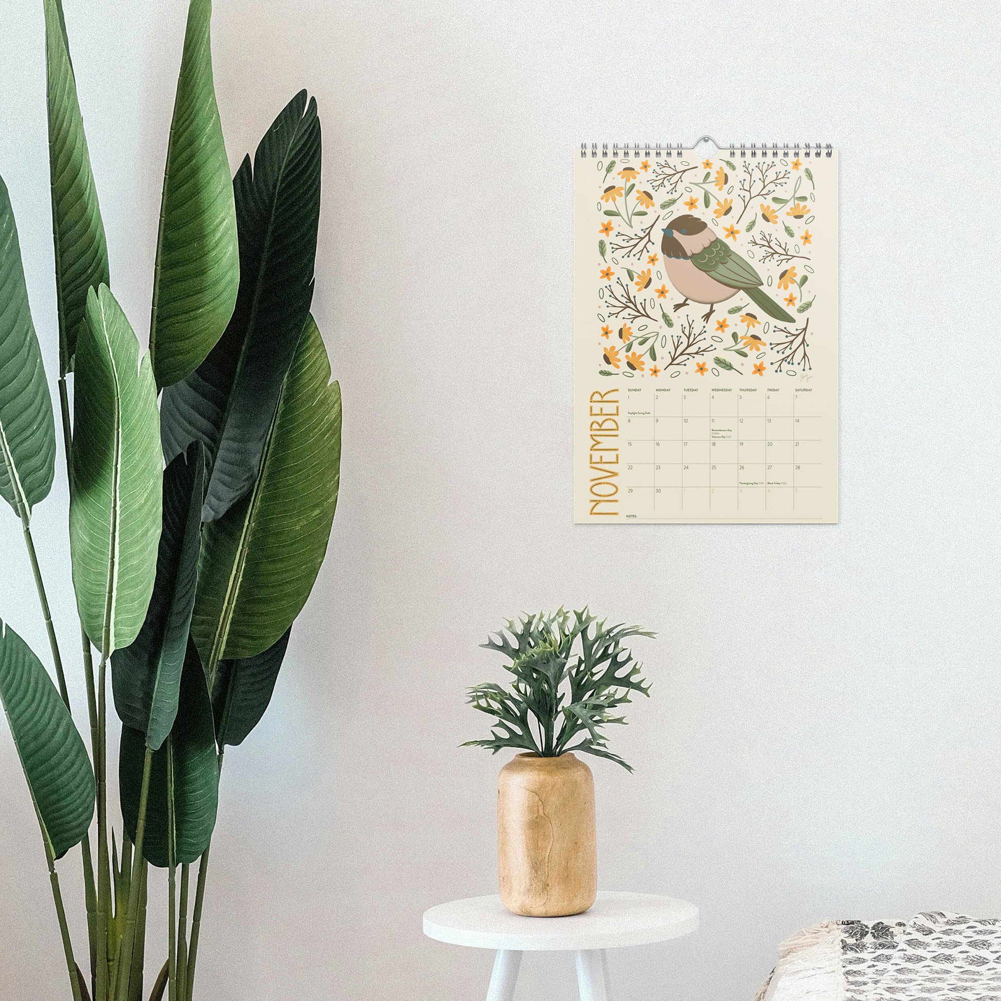 2026 wire-bound wall calendar hanging on a neutral wall, displaying colourful folk-art animal artwork and a clear monthly layout. Ideal for home offices, kitchens, studios, classrooms, or anyone looking for a decorative illustrated 2026 wall calendar with unique art.