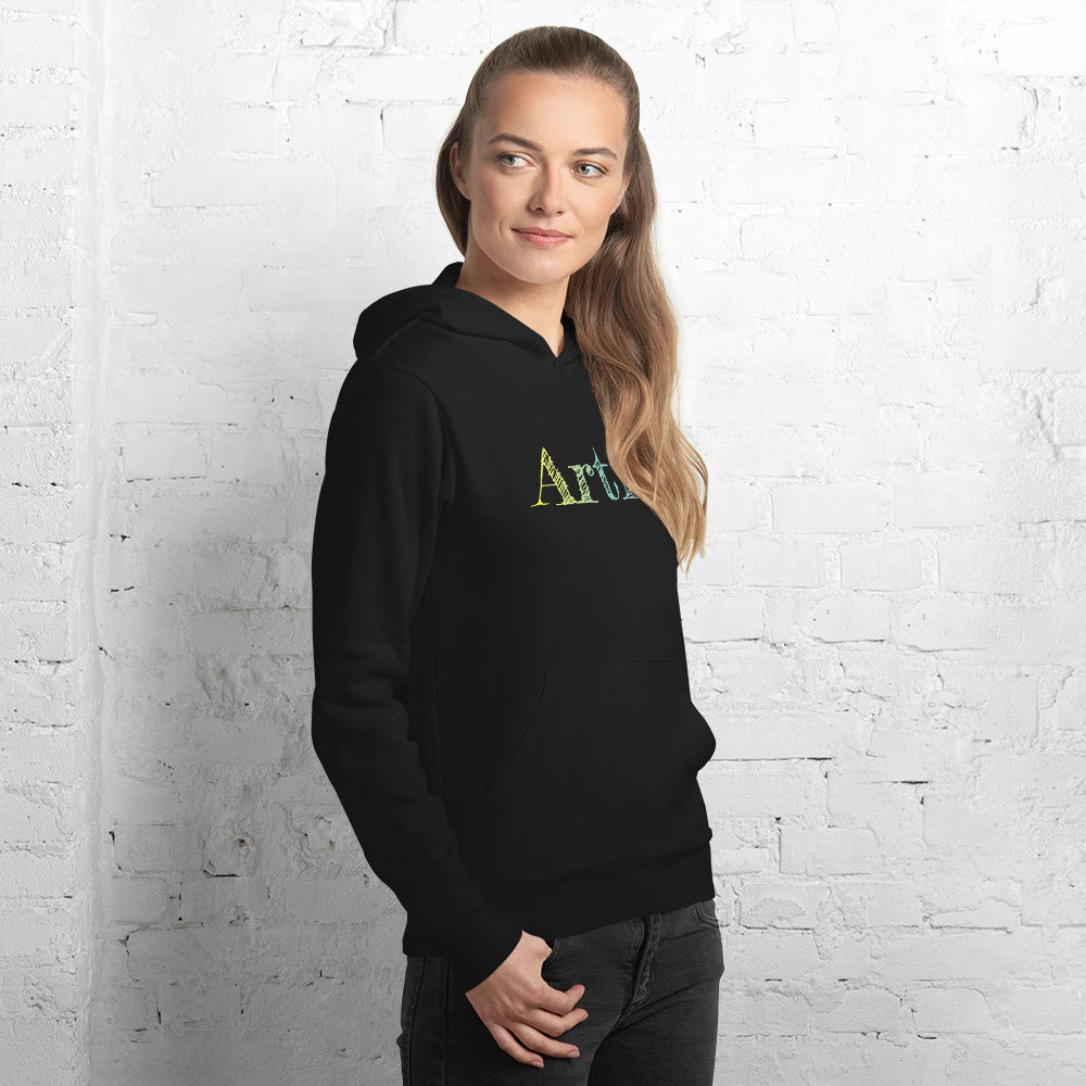 A woman models the black artist hoodie in front of a white brick wall, showing the comfortable unisex fit and the bold hand-drawn gradient text design in yellow, green and soft purple. The hoodie looks soft, cozy and perfect for everyday wear—ideal for artists, illustrators, art students and creative professionals. A great art lover gift and an aesthetic clothing choice for anyone who enjoys unique graphic apparel.